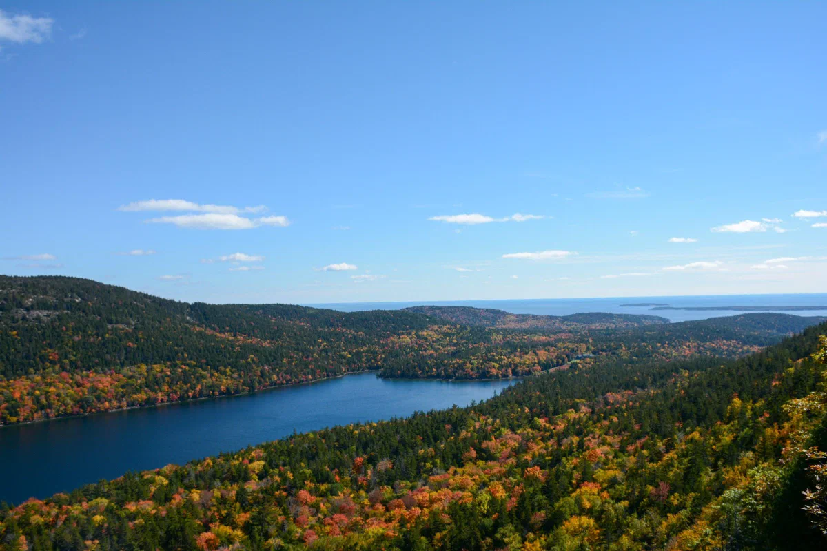 A blue lake surrounded by wooded hills in green, yellow, and orange autumn foliage.