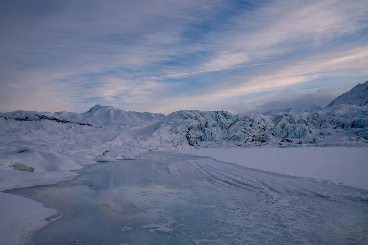 A frozen lake and snow-covered glacier beneath streaks of pale pink cloud.