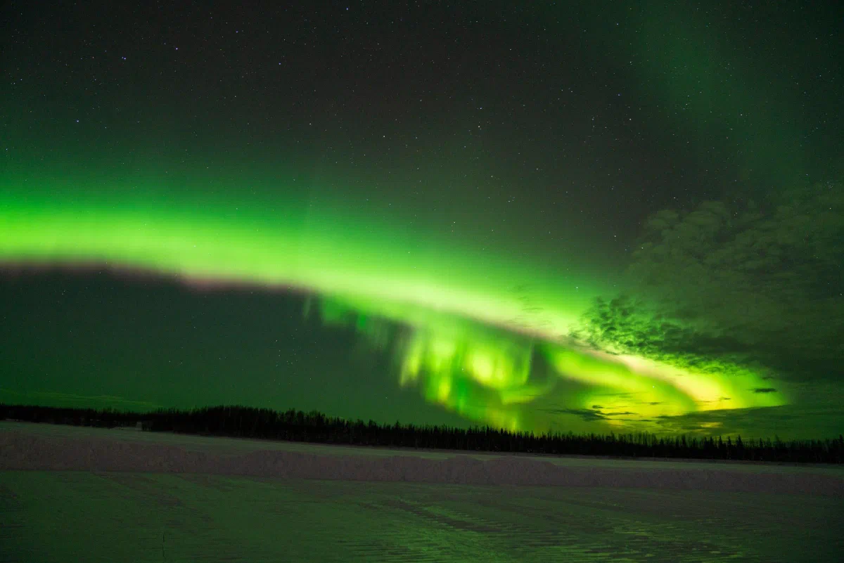 A bright green aurora stretching across the night sky above a snowy landscape.