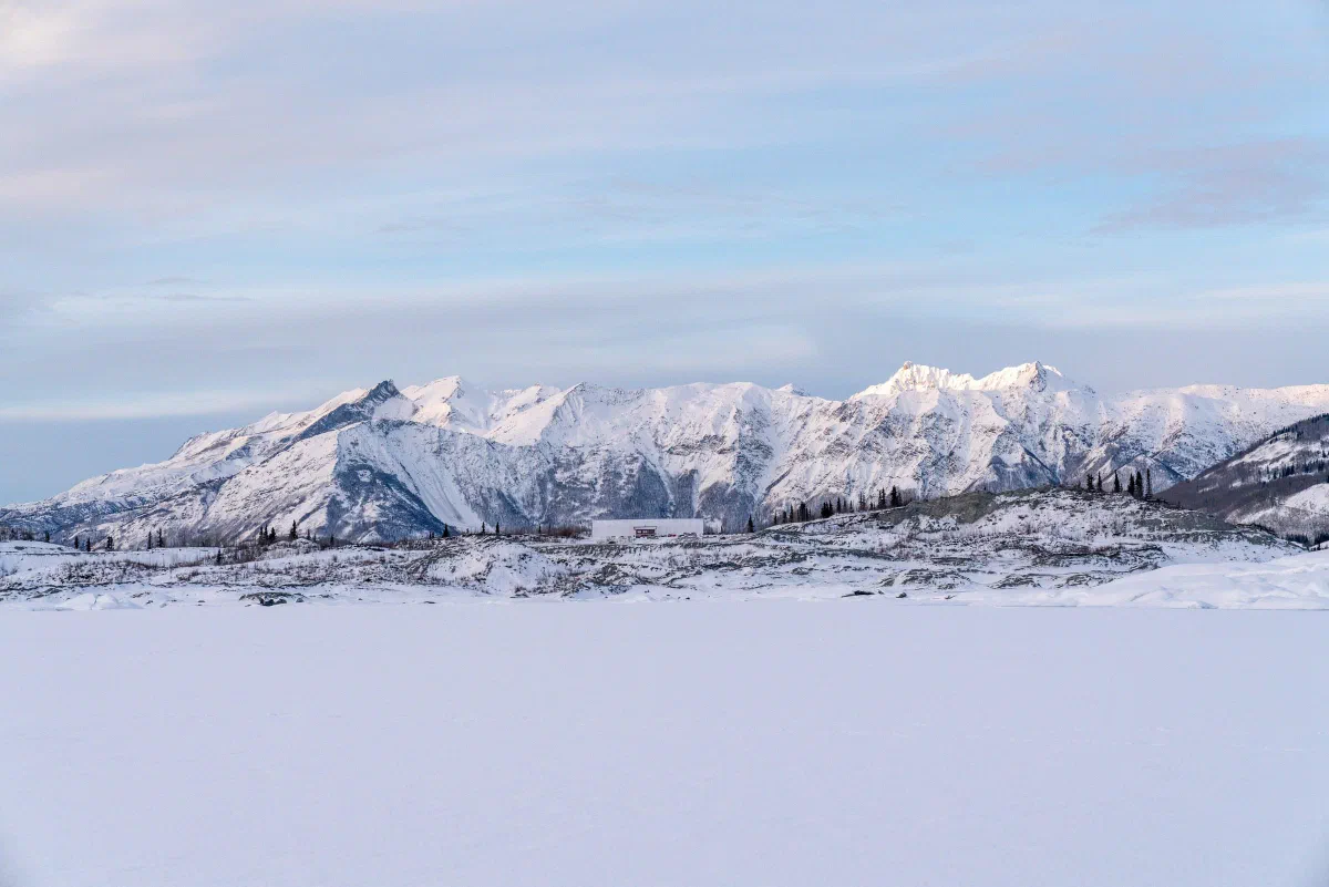 A snowy mountain range stretching across a frozen landscape beneath pale clouds.
