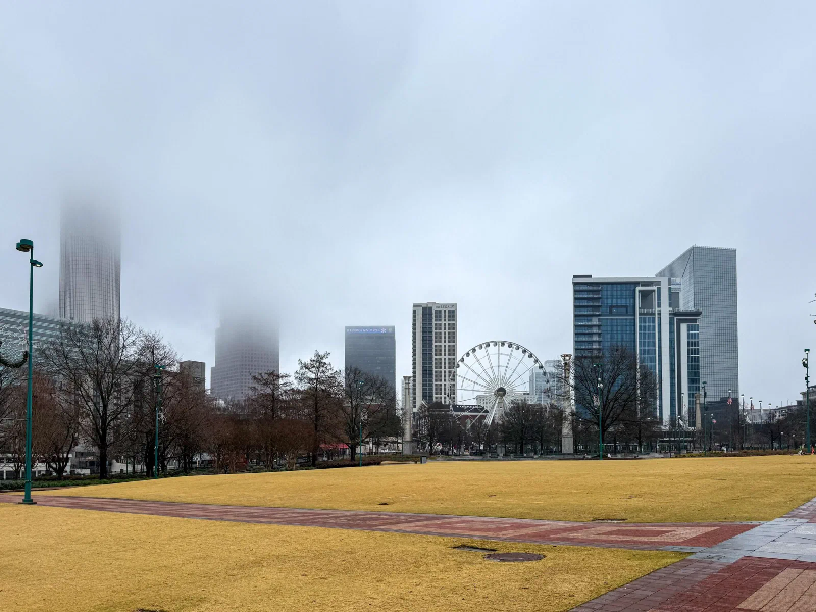 A broad plaza facing a Ferris wheel and buildings whose upper floors disappear into mist.