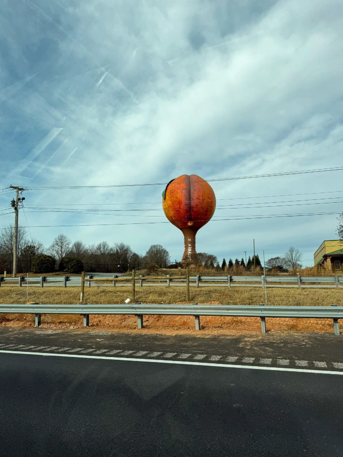 An orange spherical sculpture beside a road beneath a streaked sky.