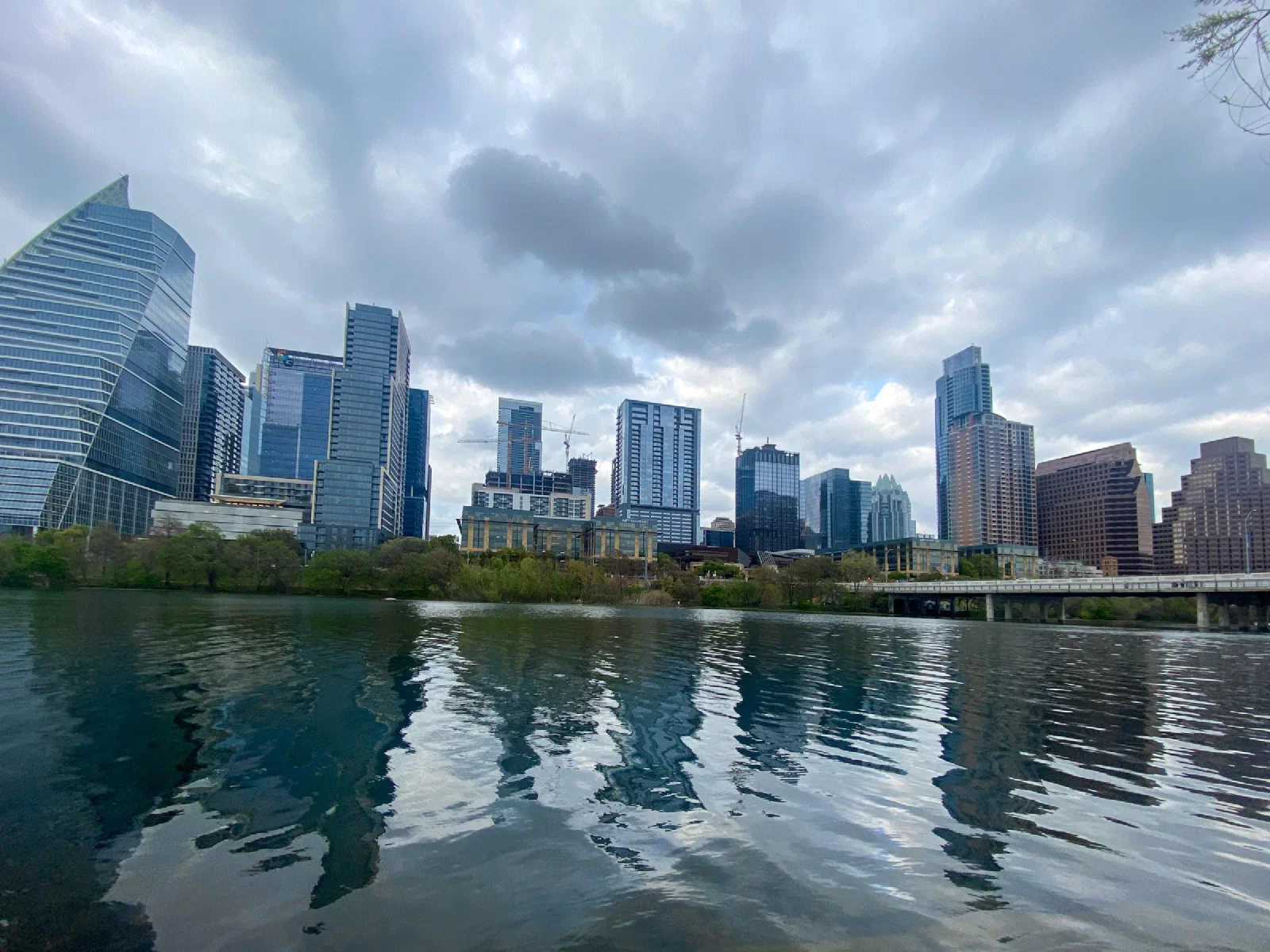A city skyline reflected in calm water under a cloudy sky.