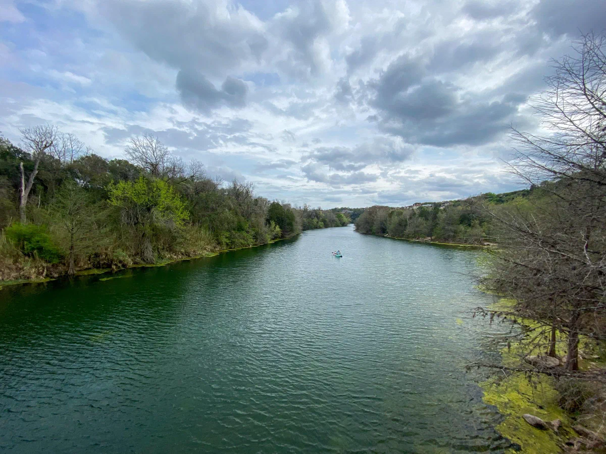 A broad river bordered by trees beneath a sky filled with gray clouds.