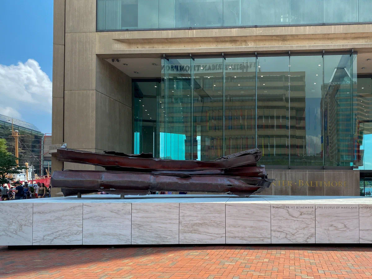 A long dark sculpture in front of a glass entrance and a pale stone wall.