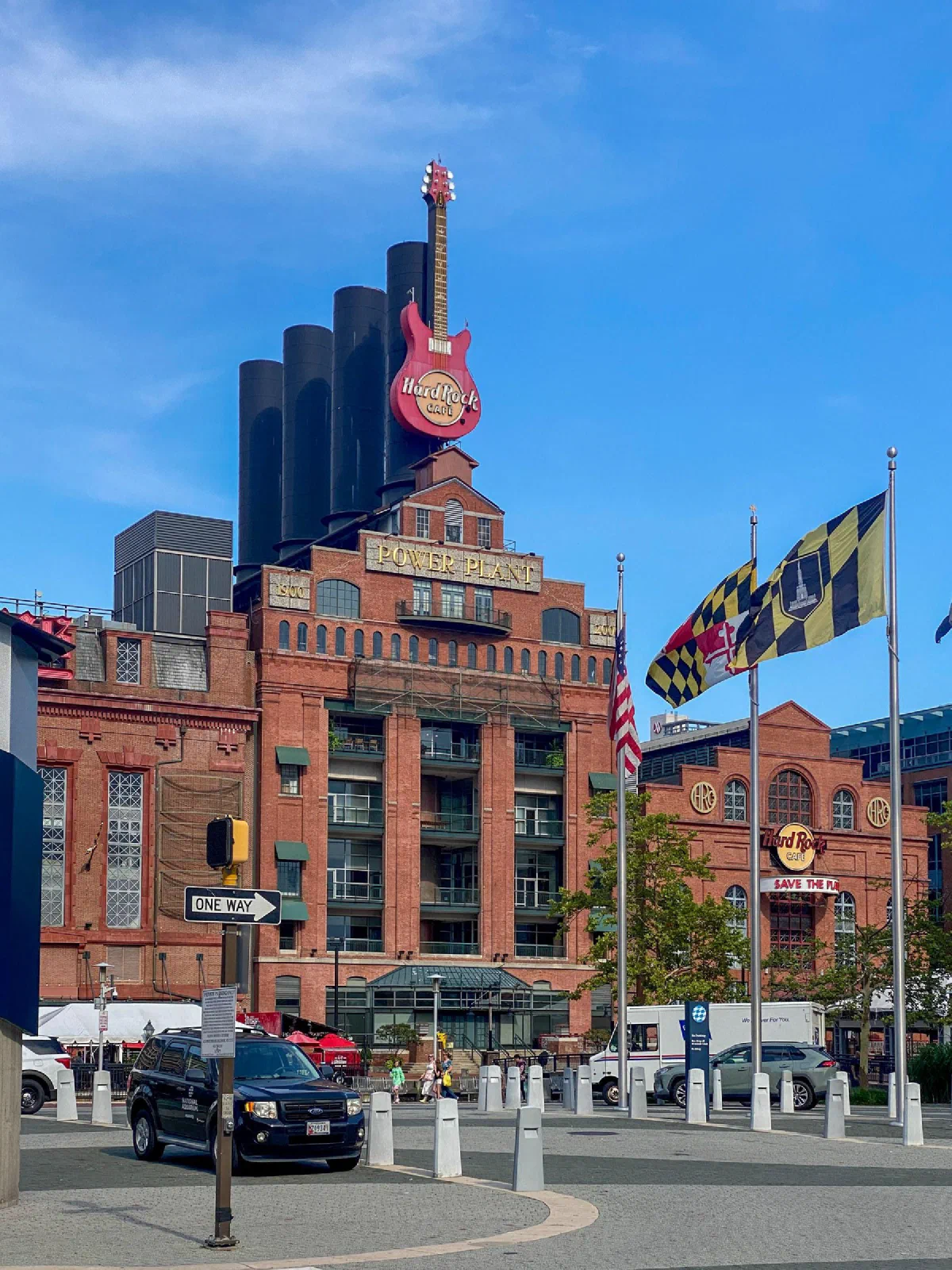 A large guitar sign above a brick building, with flags beside the street.