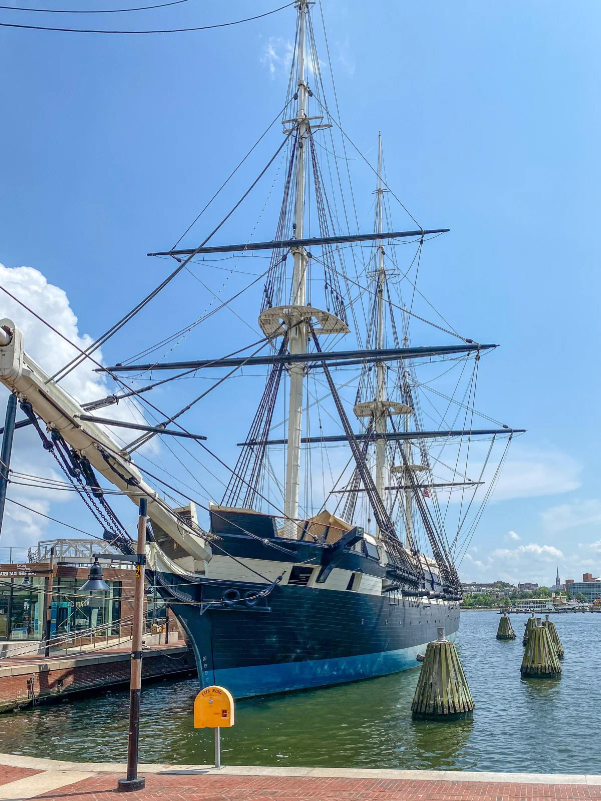 A tall sailing ship with rigging and a dark hull moored beside a waterfront walkway.