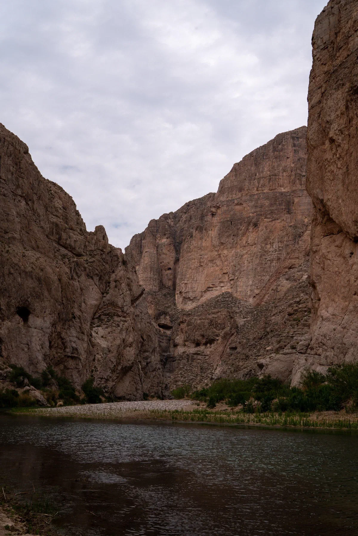 A narrow river running between tall, rugged canyon walls beneath a gray sky.