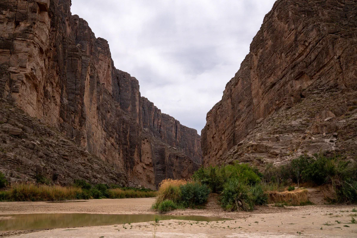A sandy riverbank and green shrubs enclosed by steep canyon walls.
