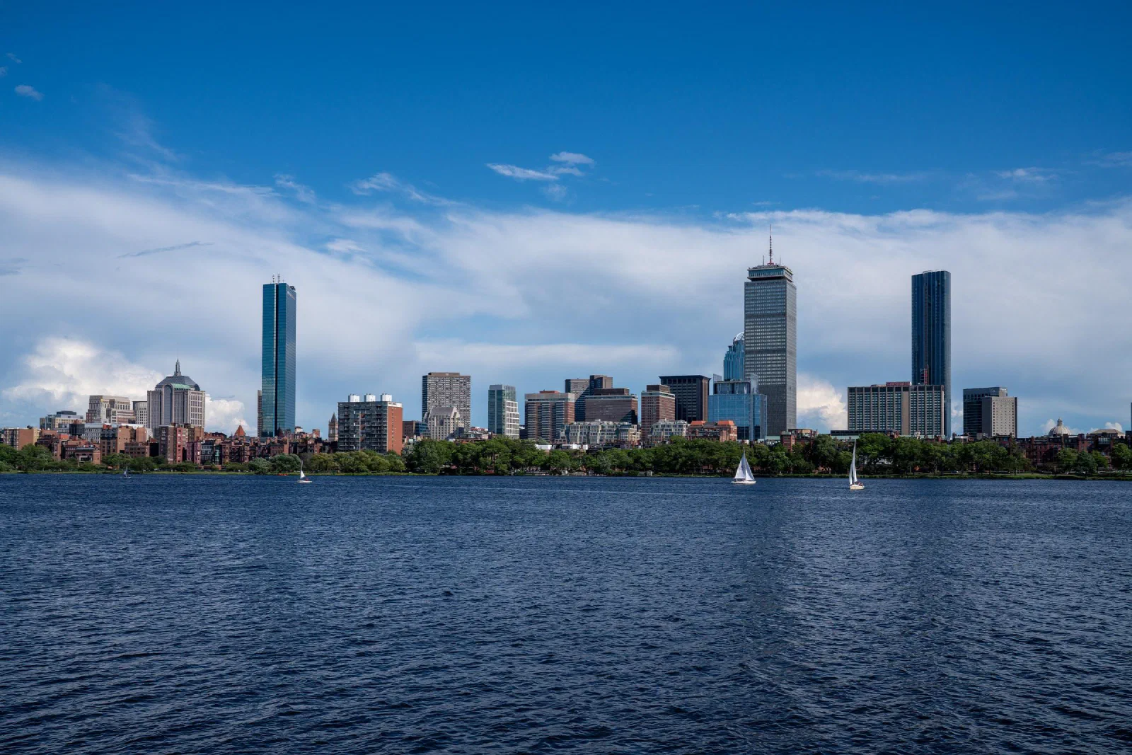 The city skyline across blue water, with small sailboats on the river.