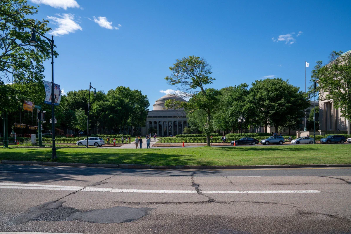A domed building beyond a broad lawn and trees, viewed across a city street.