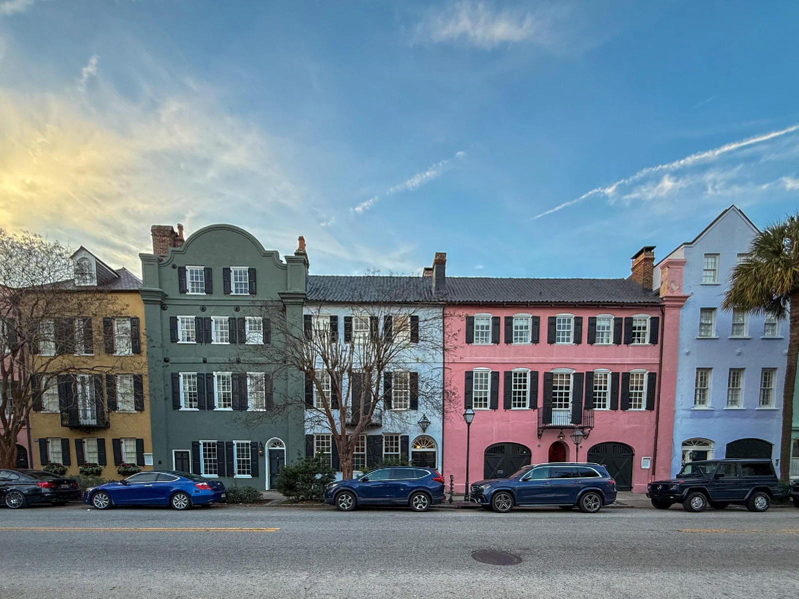 A row of narrow houses with green, pink, and pale facades beneath wispy clouds.