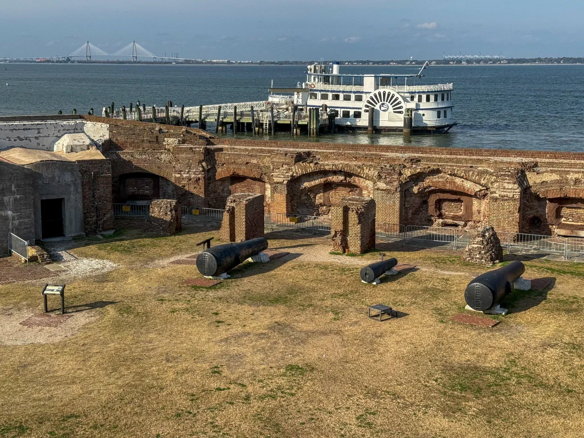 Cannons and brick fortifications beside the water, with a white boat beyond.