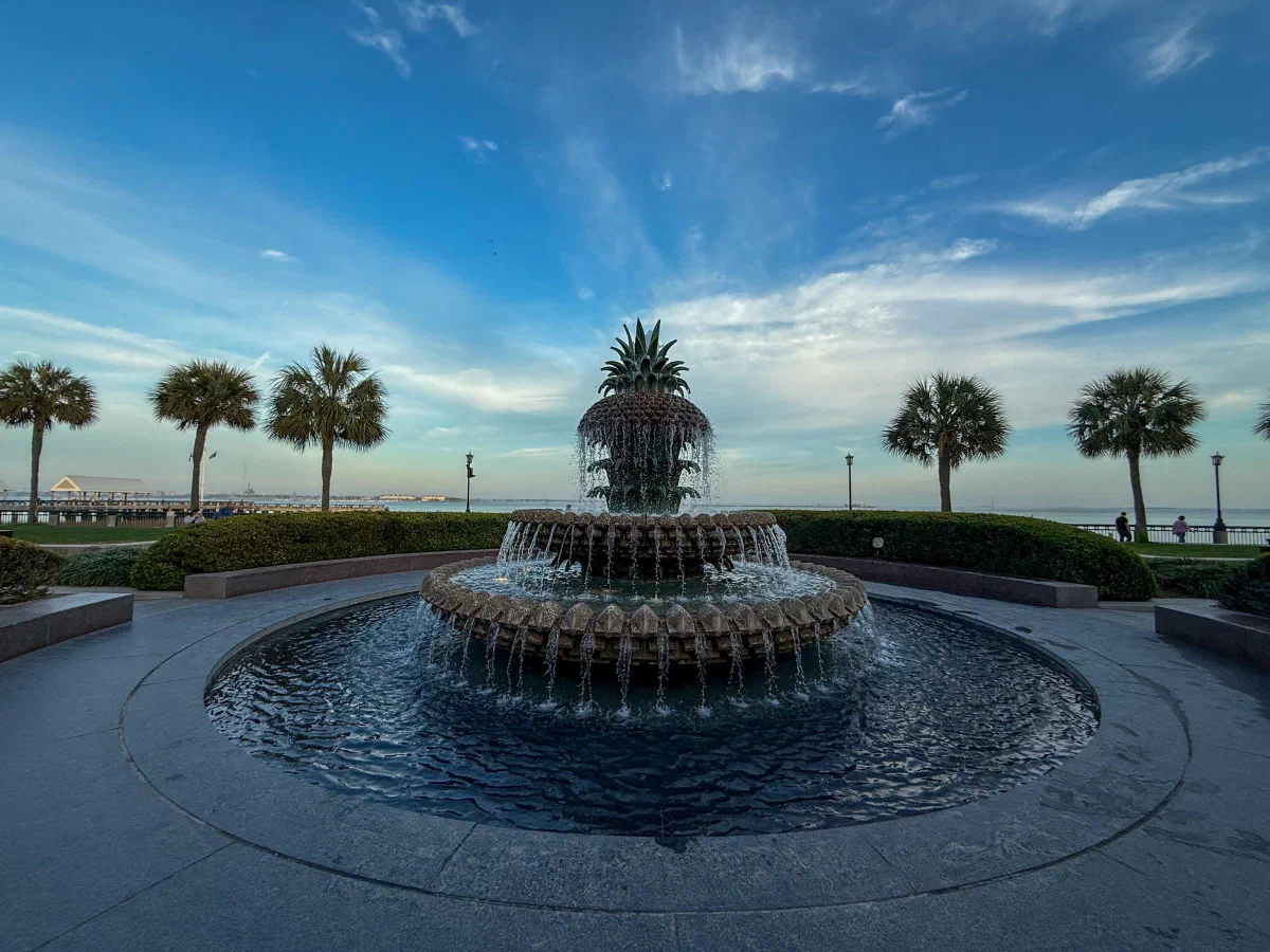 A pineapple-shaped fountain surrounded by palm trees beside the waterfront.