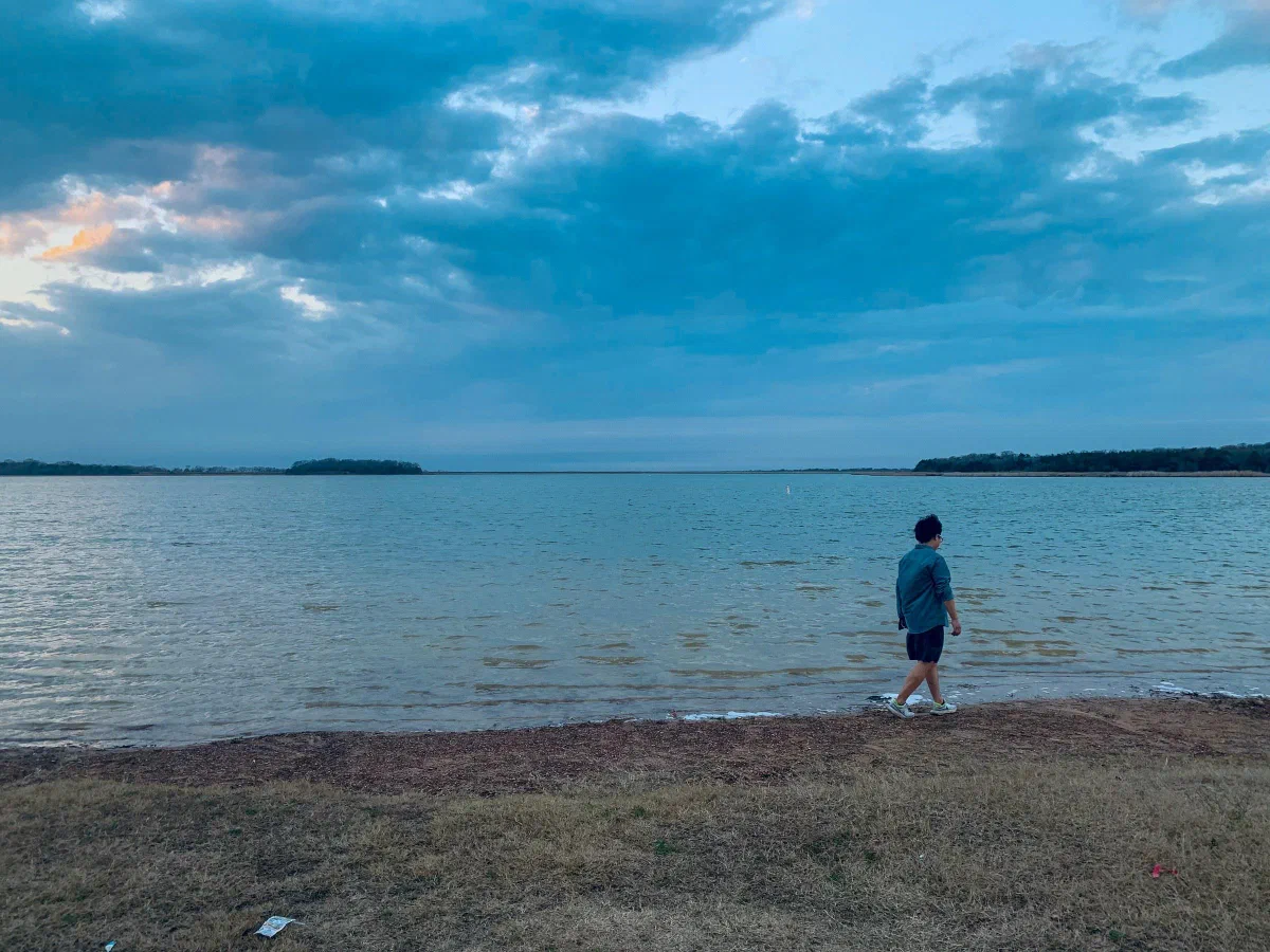 A person walking along the shore of a lake beneath a blue evening sky.