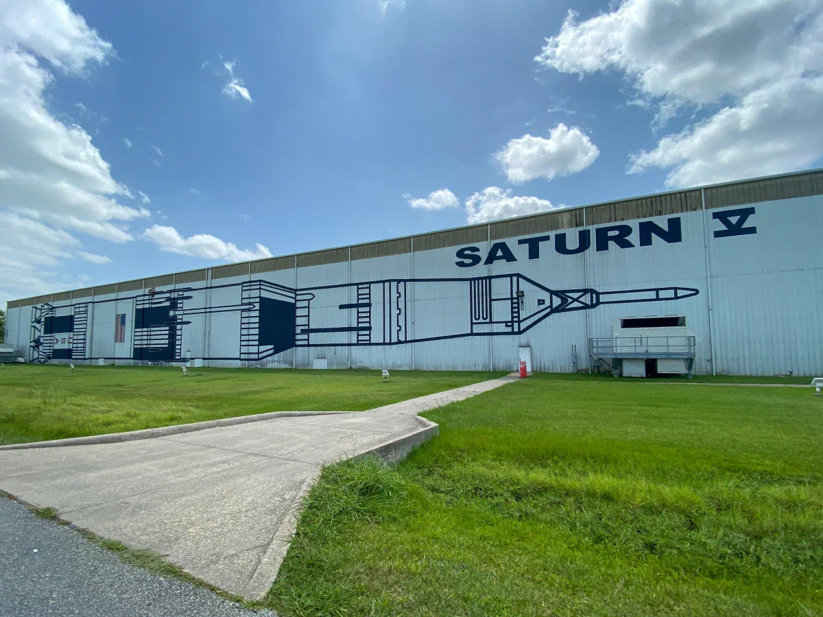 A low building marked Saturn V beside a concrete path and green lawn.