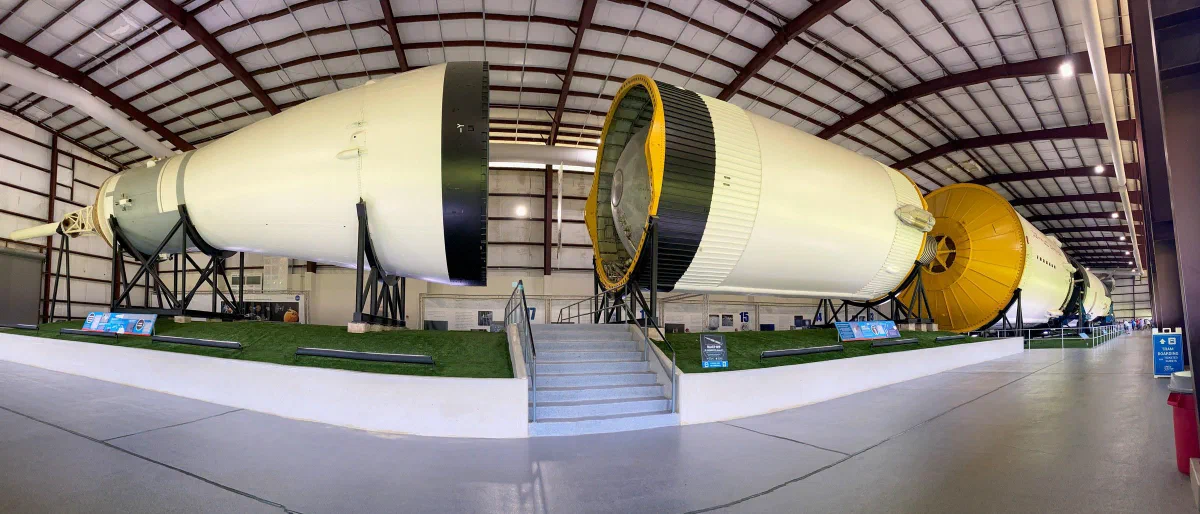Large rocket stages displayed inside a hangar with exposed roof beams.