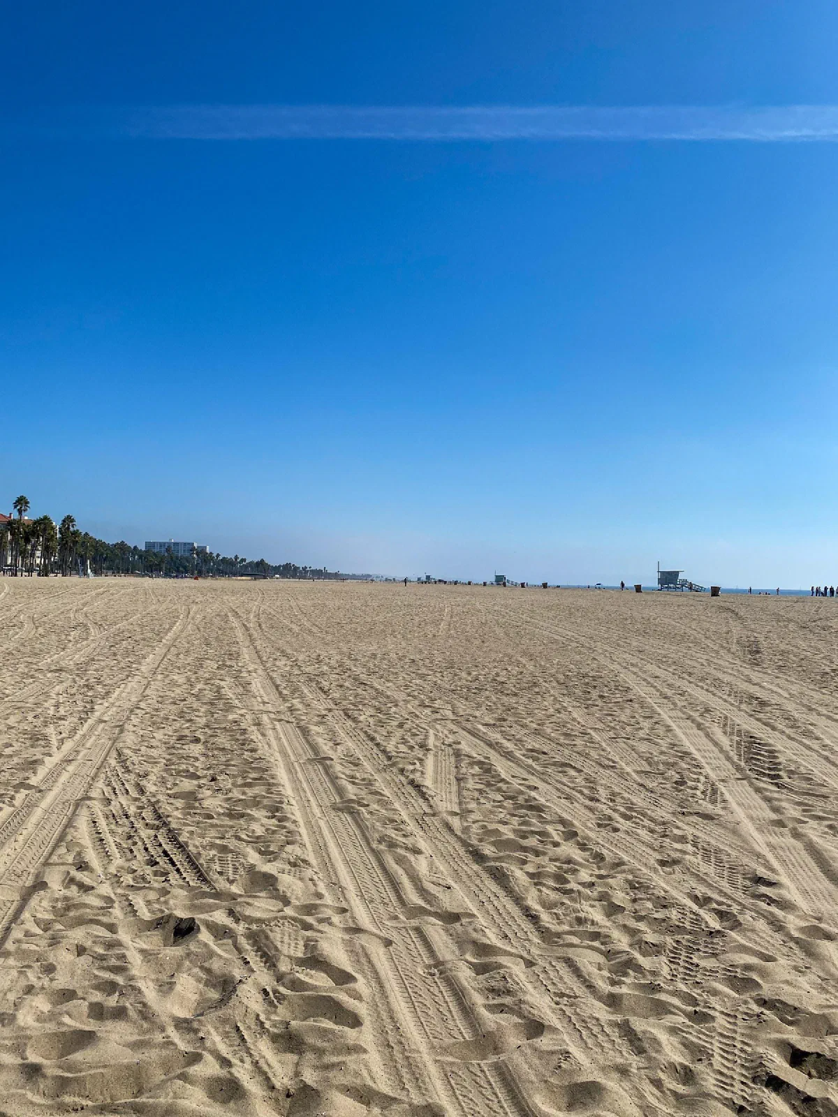 A broad sandy beach covered in parallel tracks beneath a blue sky.