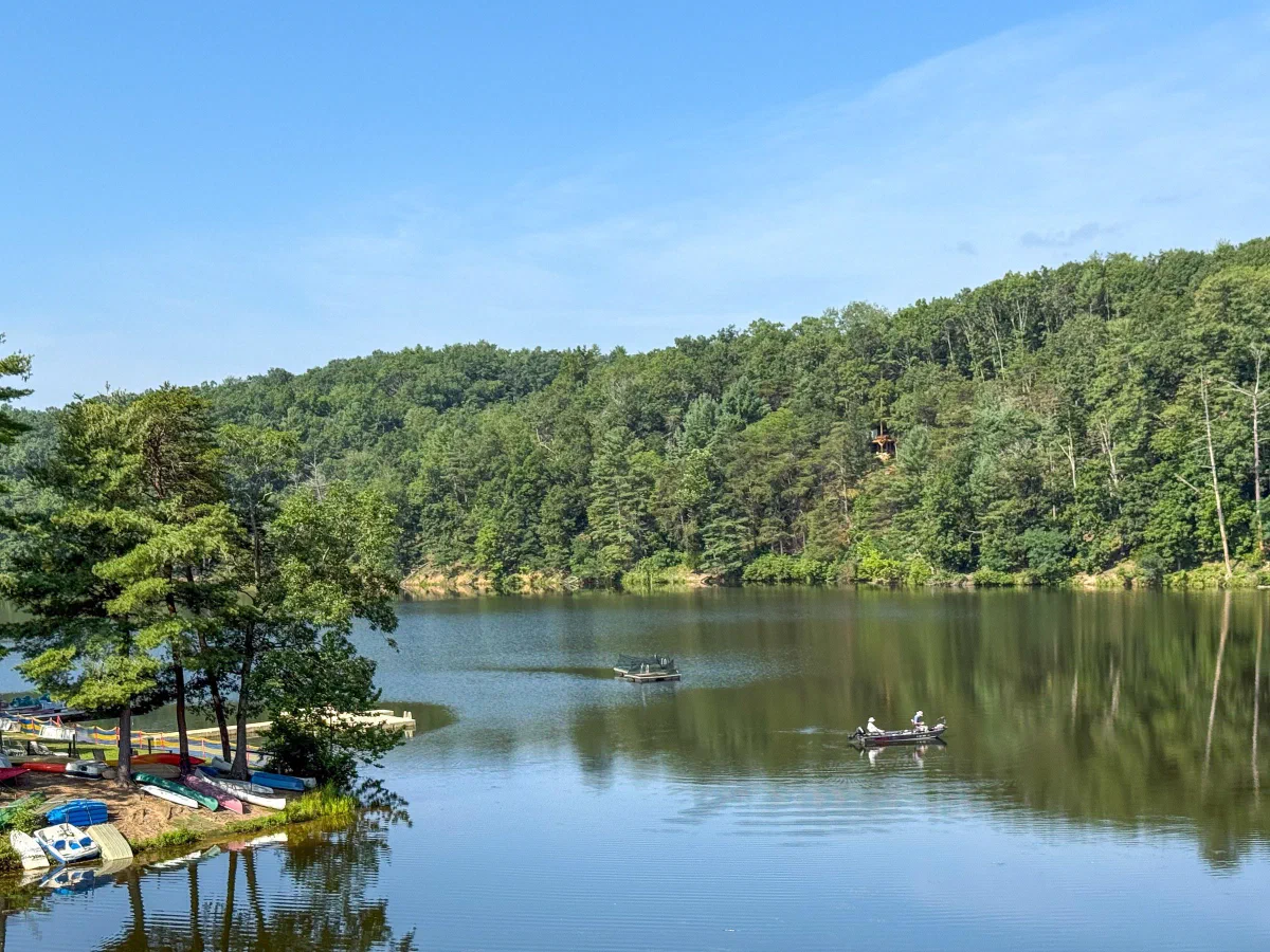 A small boat on a calm lake bordered by green hills, with a dock along the shore.