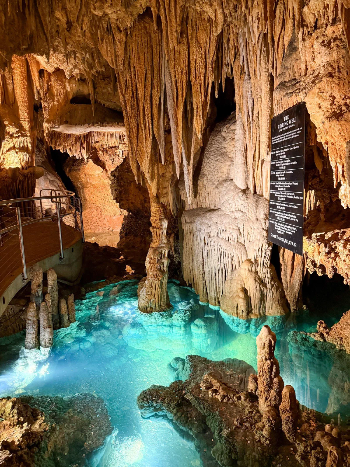 Stalactites and rock columns above a brightly illuminated turquoise pool in a cavern.