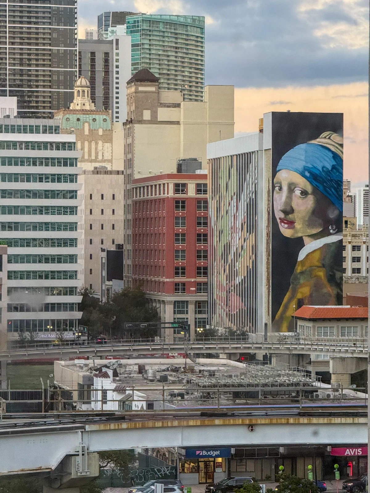 A large portrait of a woman in a blue head covering on a wall among city buildings.