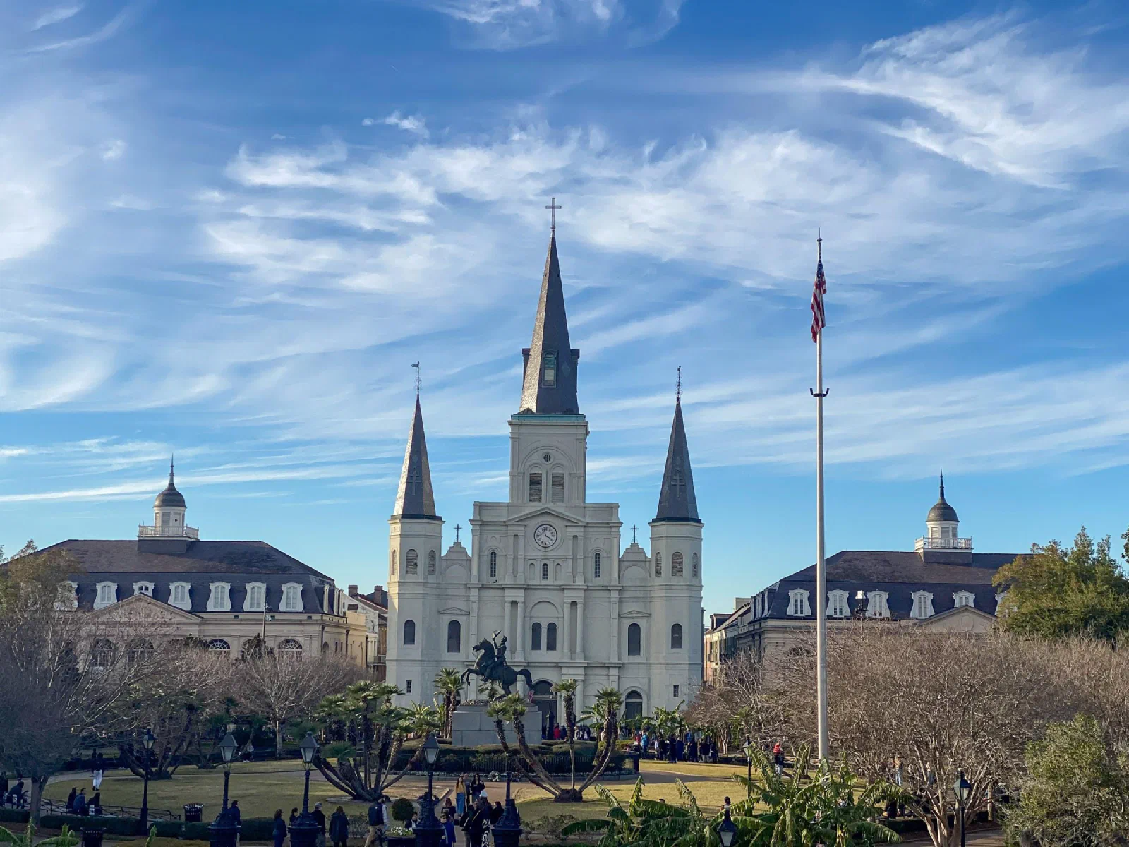 A white cathedral with three pointed spires behind a garden and a crowd of people.