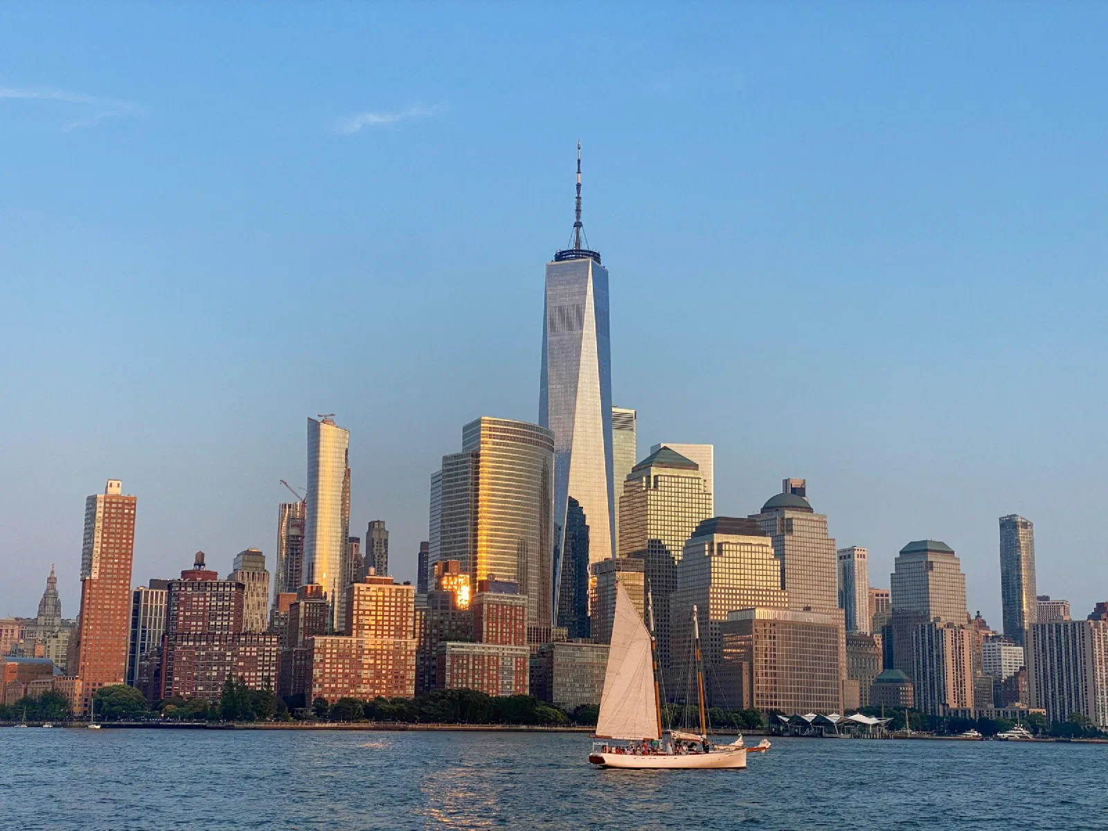 A sailboat on the water in front of the Manhattan skyline in evening light.