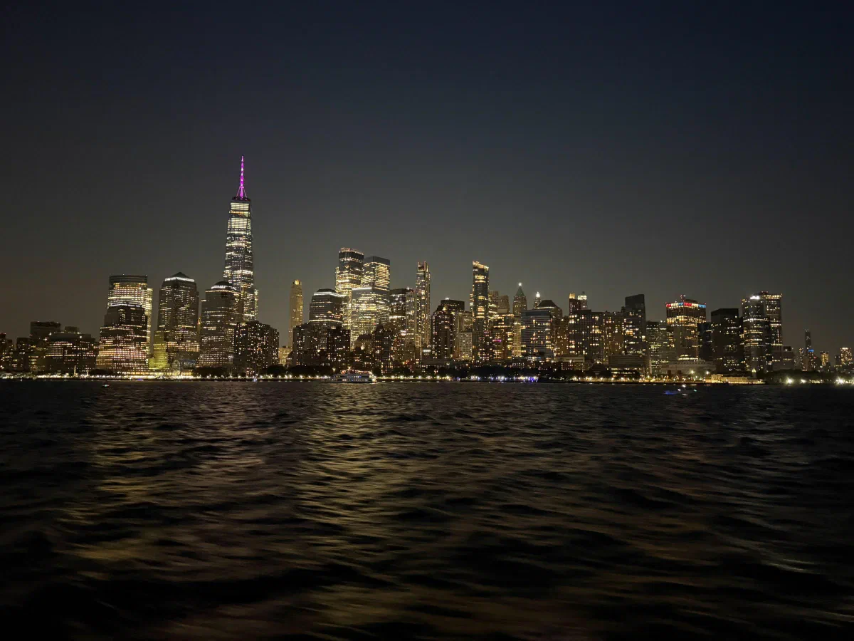 An illuminated city skyline across dark water beneath the night sky.