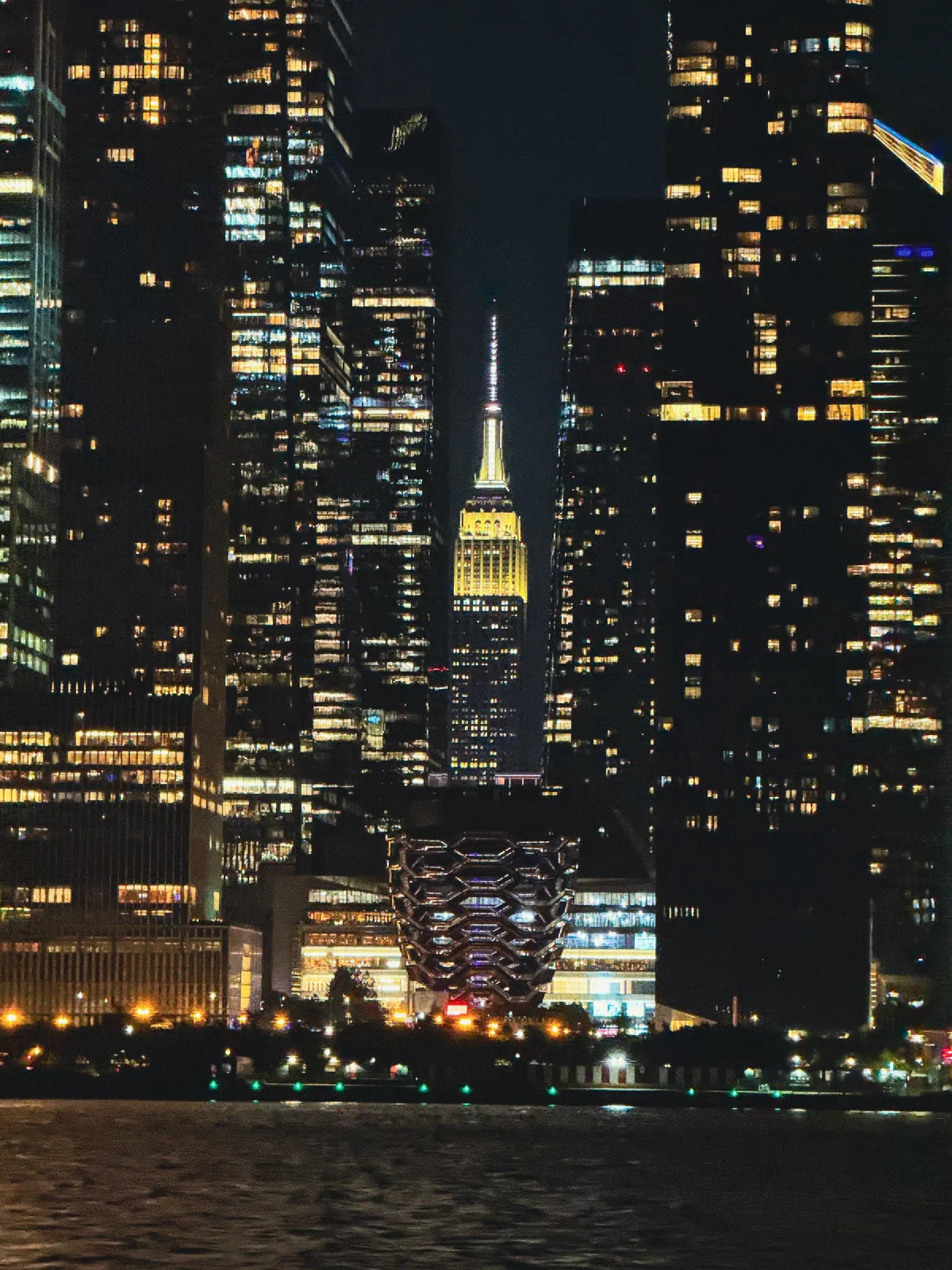 An illuminated pointed skyscraper framed by taller dark buildings at night.