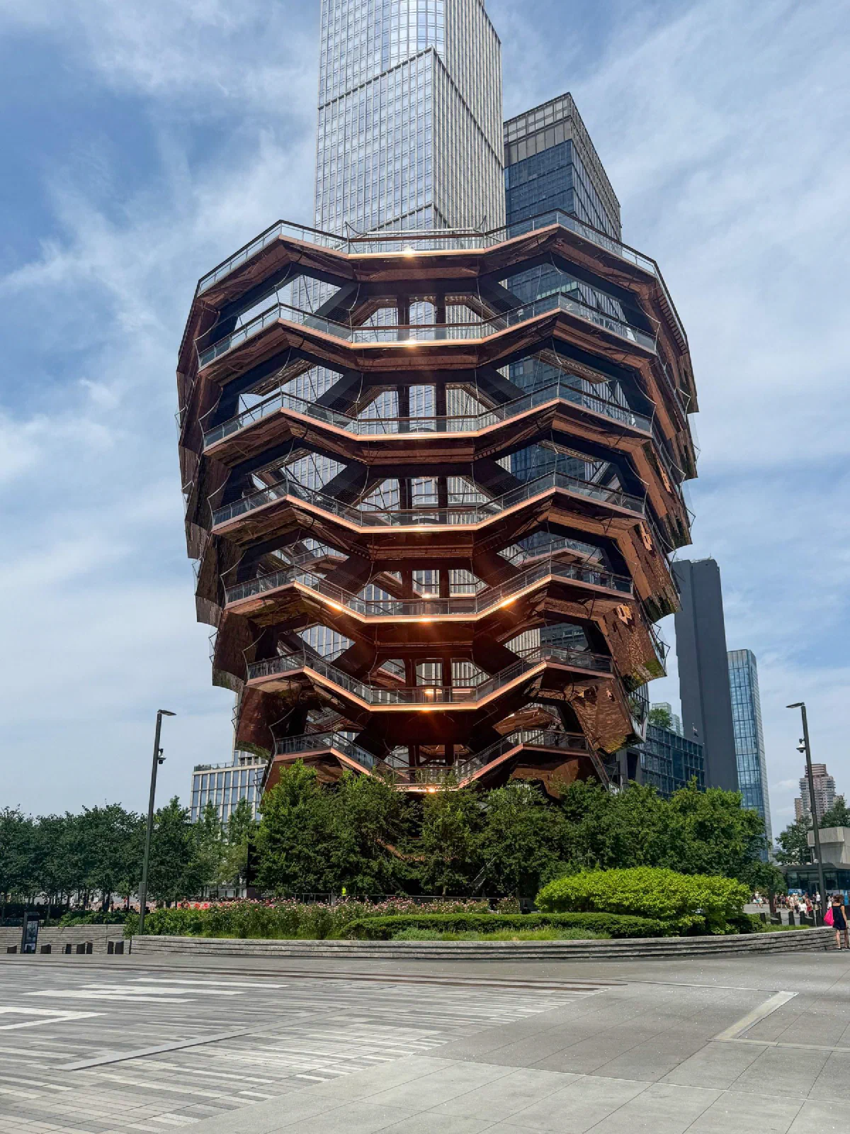 A copper-colored structure of interlocking stairways in front of tall glass buildings.