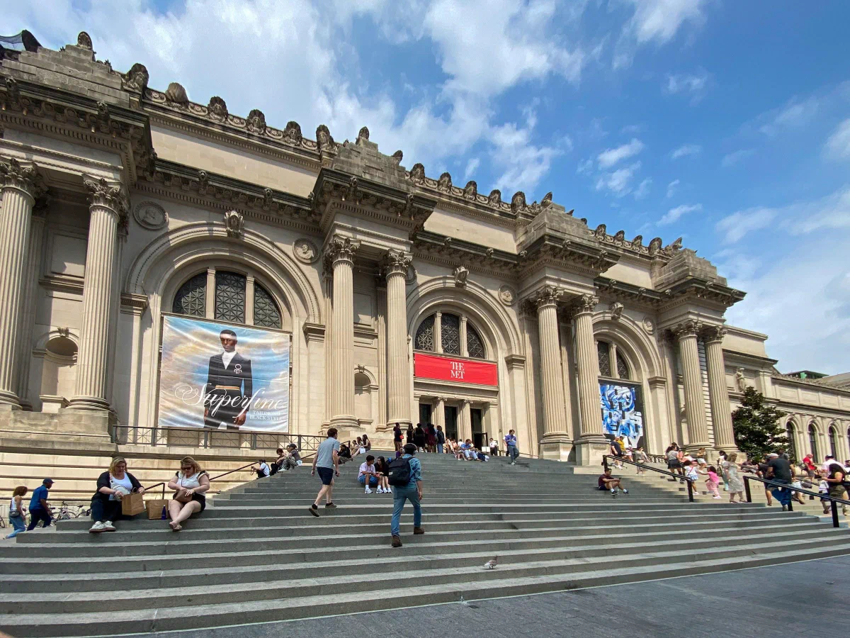 Visitors on wide steps beneath the columns and arched windows of an art museum.