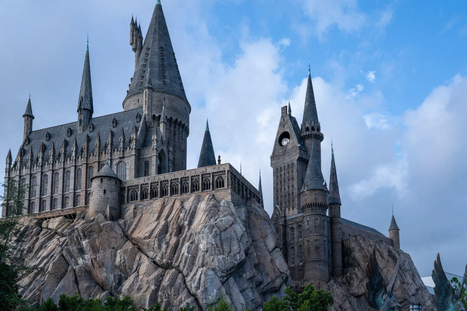 A castle with tall pointed towers built above a rocky cliff beneath a blue sky.