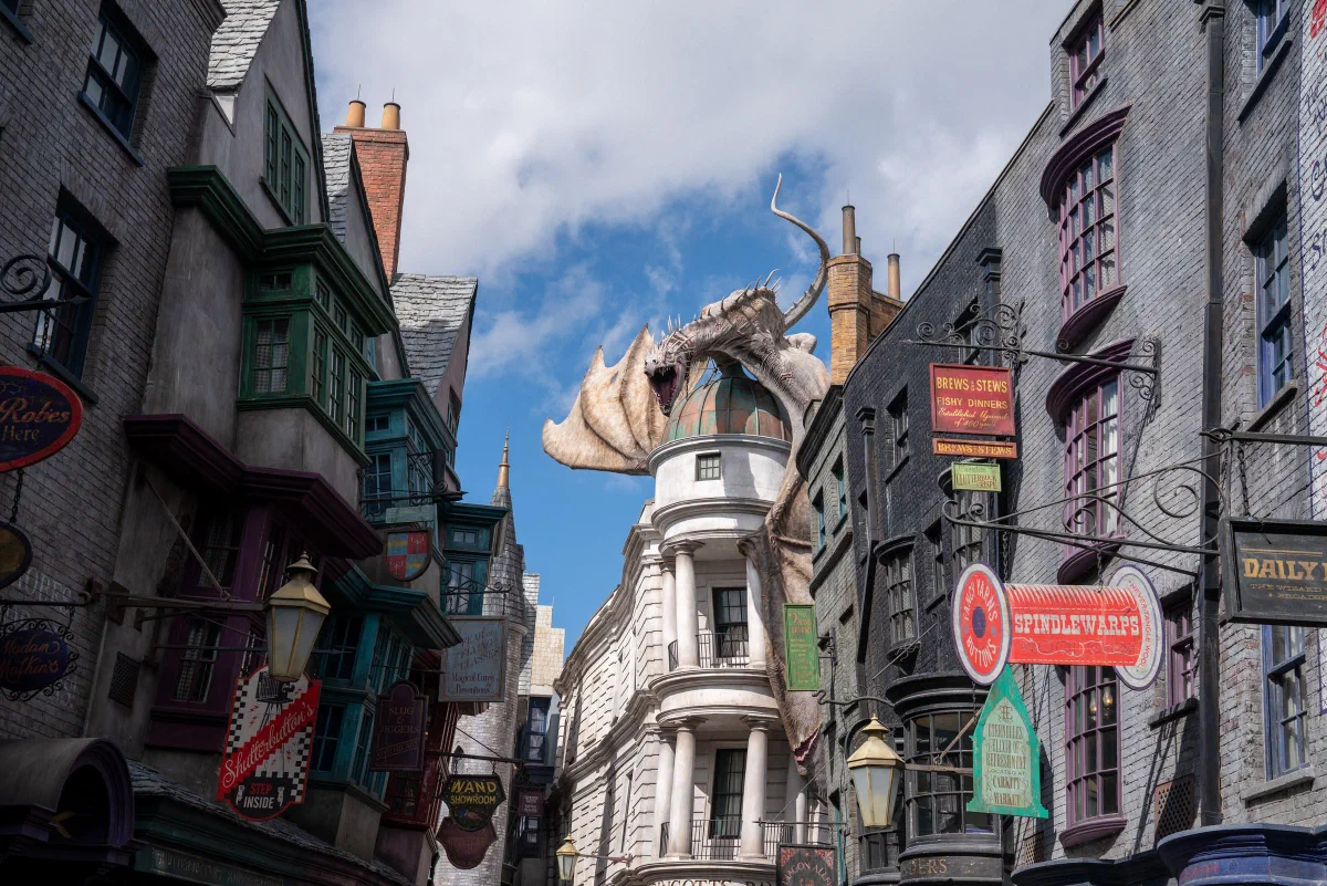 A narrow street of irregular storefronts with a dragon sculpture perched above a domed building.