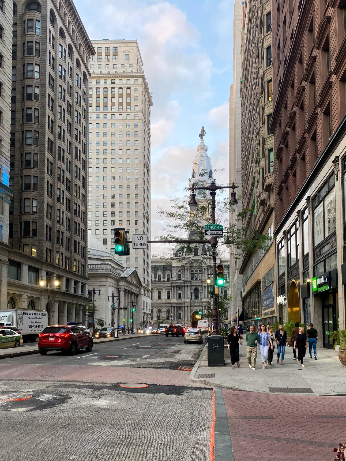 A city street lined with tall stone buildings, with a clock tower in the distance.