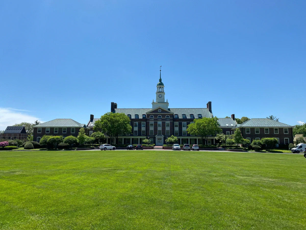 A long building with a central tower beyond a large green lawn.