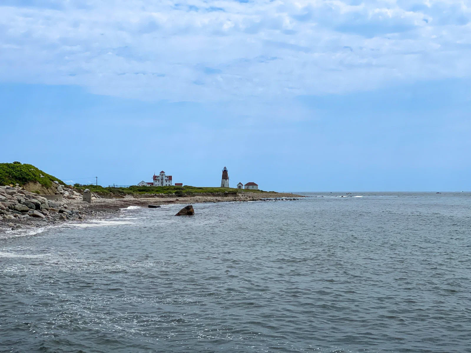 Small waves breaking along a rocky coastline beneath a blue sky.