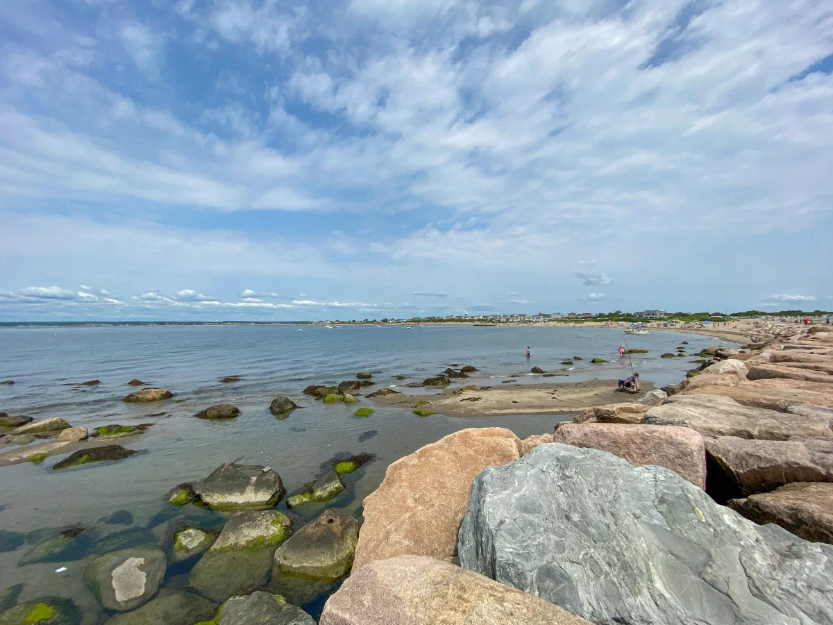 Large shoreline boulders beside calm, shallow water under streaks of white cloud.