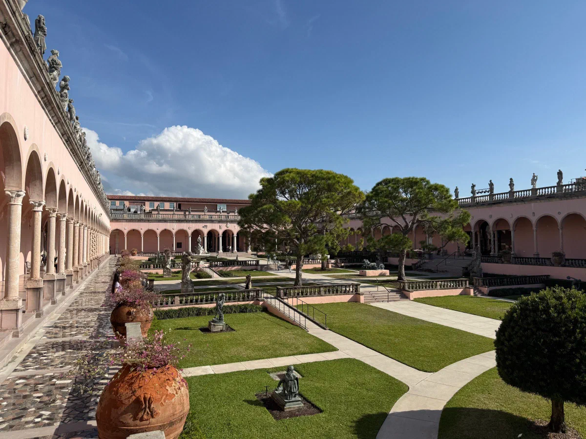 A formal garden courtyard bordered by arcades, with a large urn in the foreground.