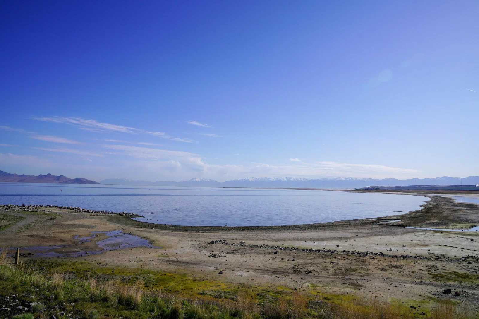 A broad lake and pale shoreline with distant mountains beneath a clear sky.