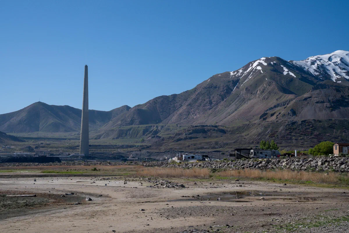 A tall narrow monument standing on open ground before mountains with patches of snow.
