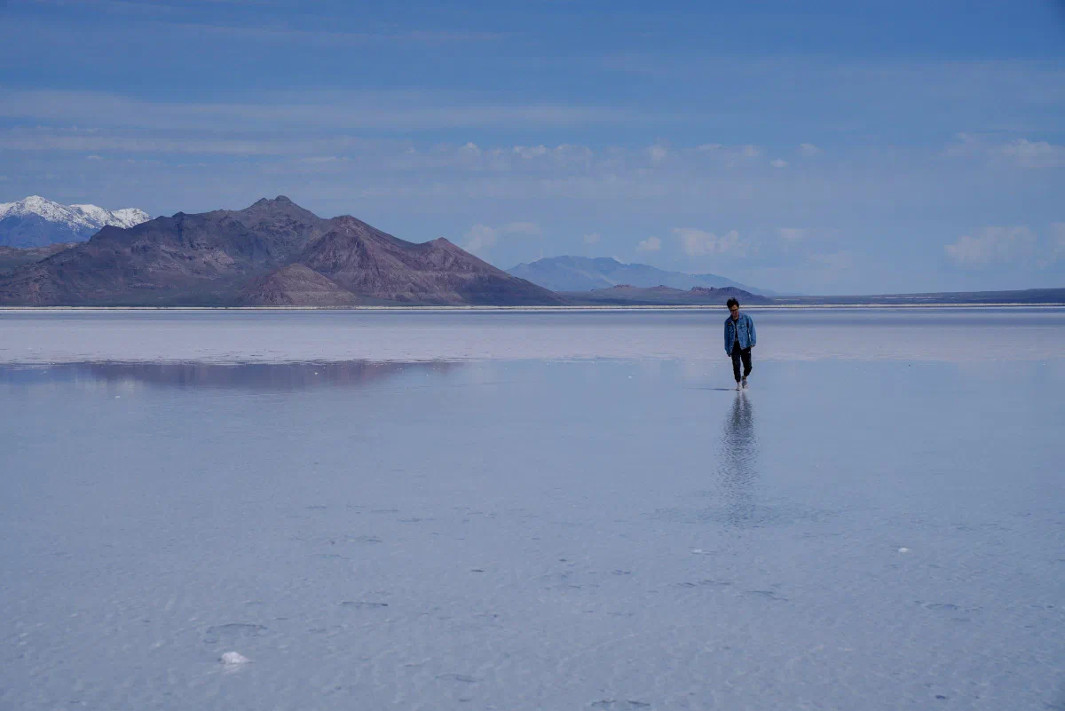 A person standing on a reflective shallow surface with mountains across the horizon.