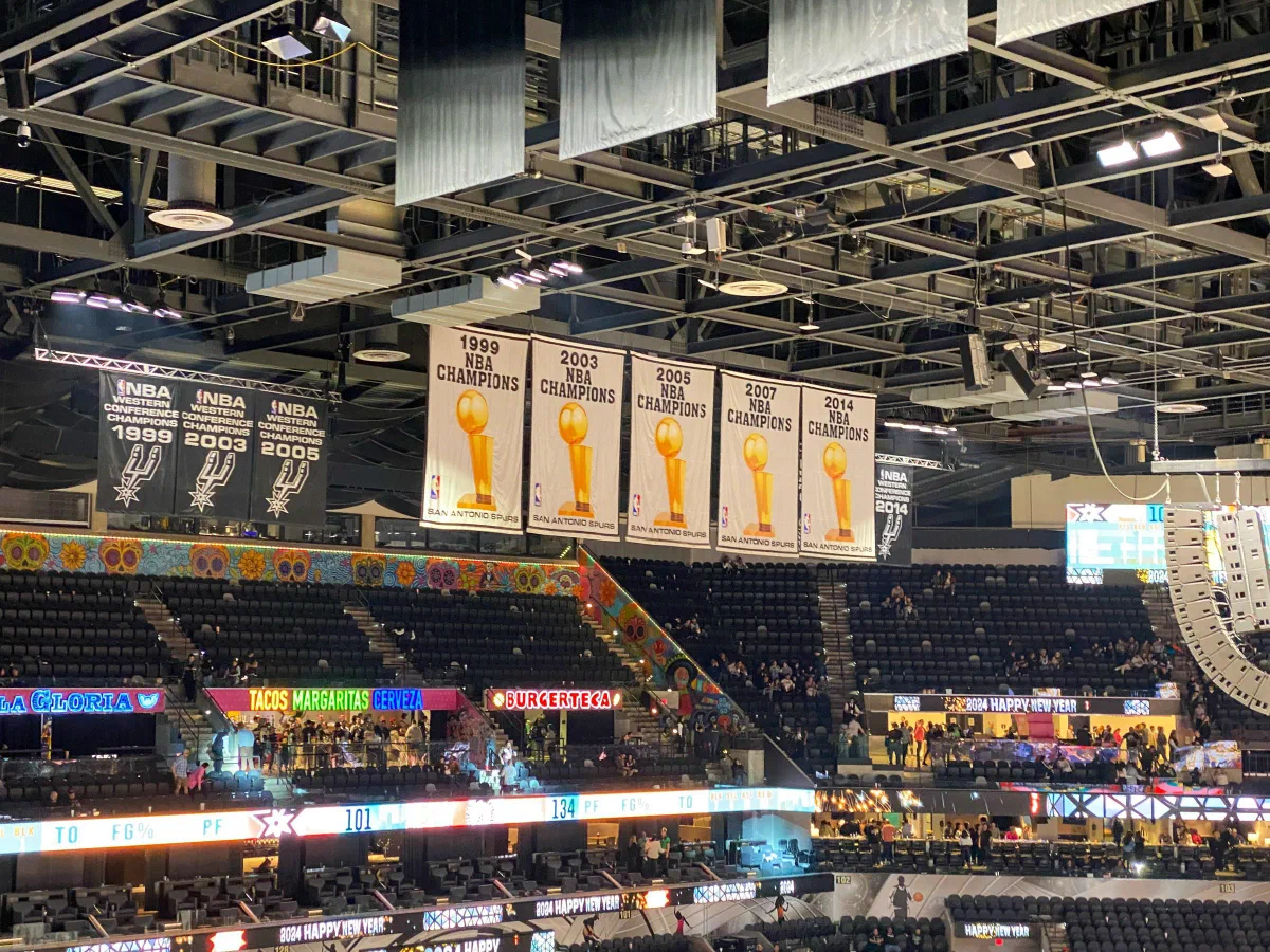 Championship banners hanging above the seats and illuminated displays of a basketball arena.