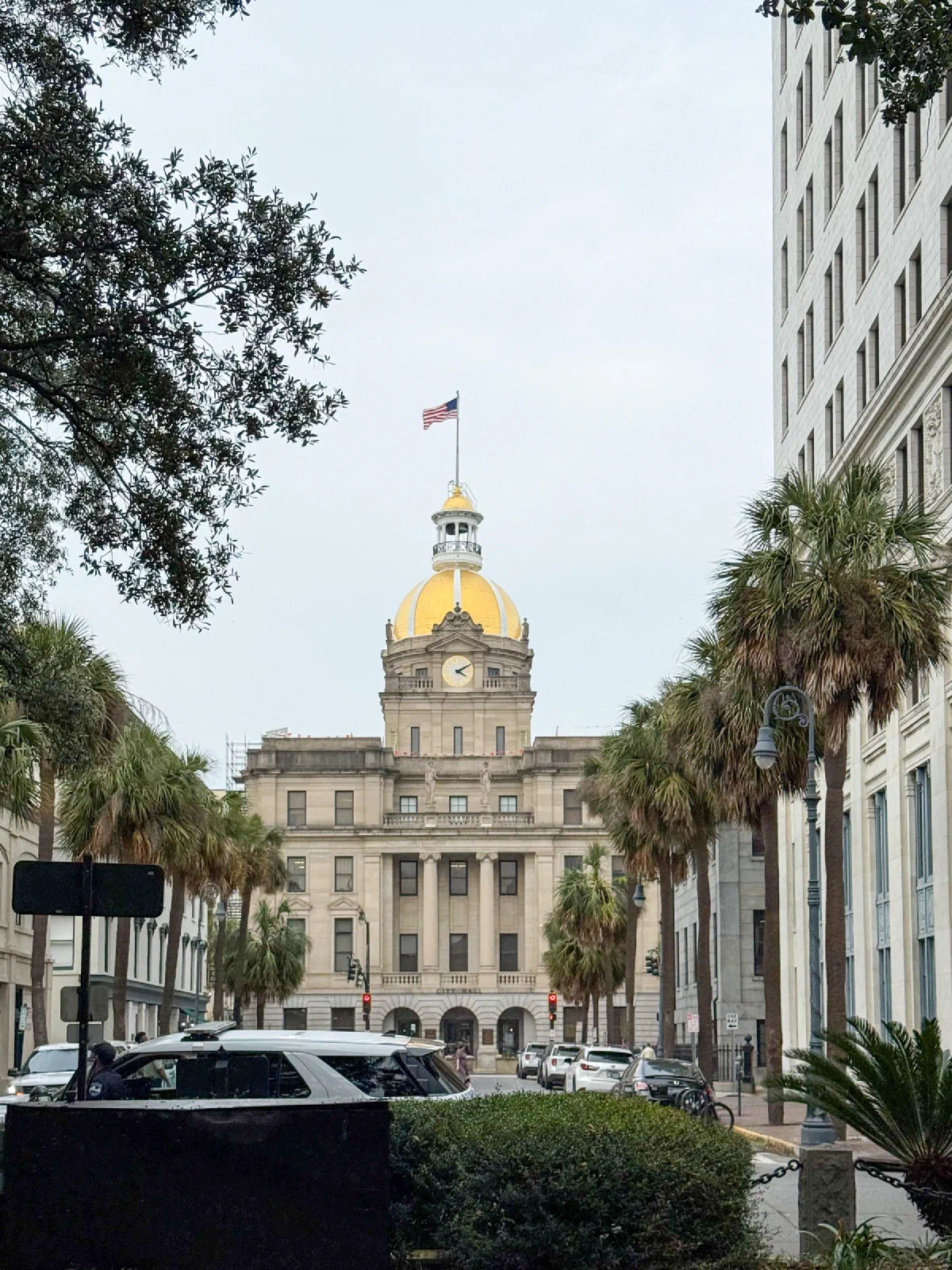 A pale building with a gold dome at the end of a street lined with trees and parked cars.