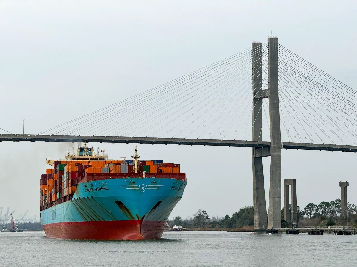 A loaded container ship passing beneath a tall cable-stayed bridge.