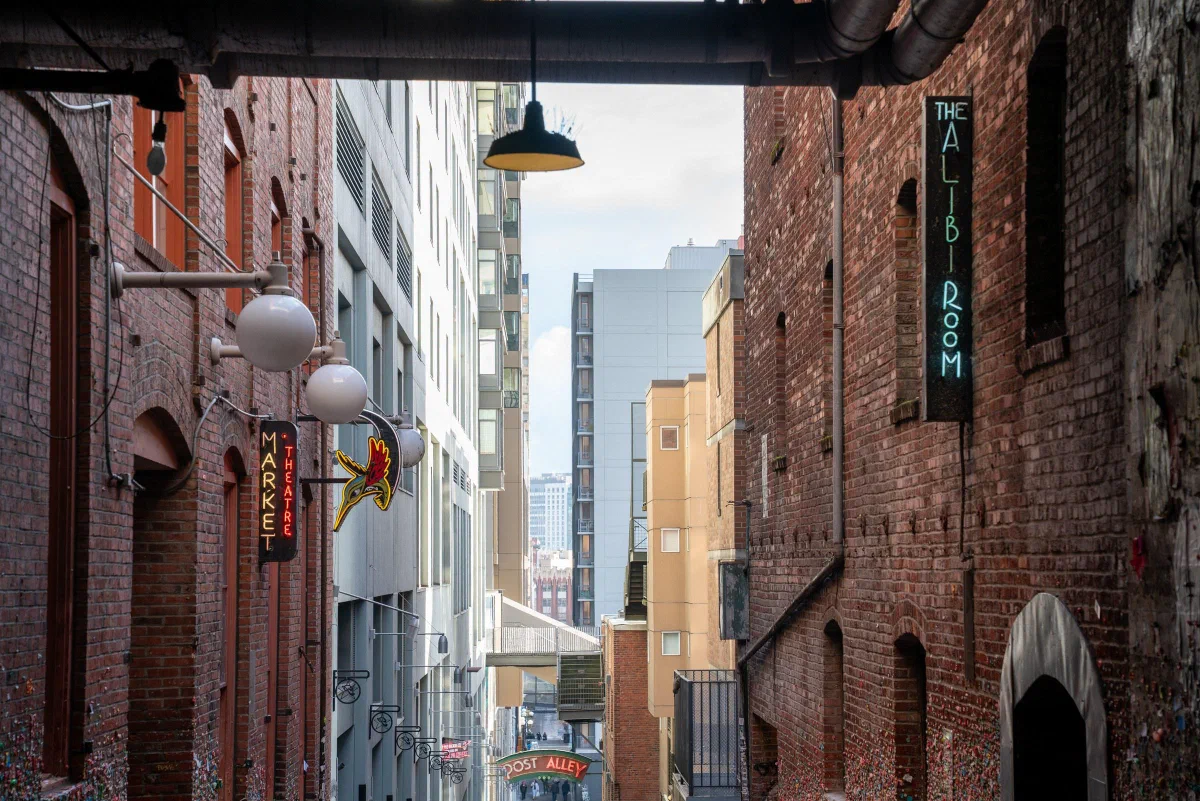 A narrow city passage between brick buildings, opening toward taller buildings.