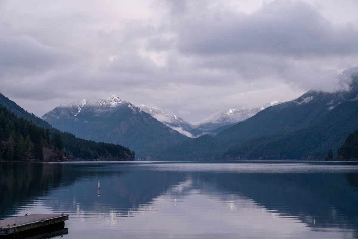 Mountains and dark clouds reflected in a still lake, with a small dock at the shore.