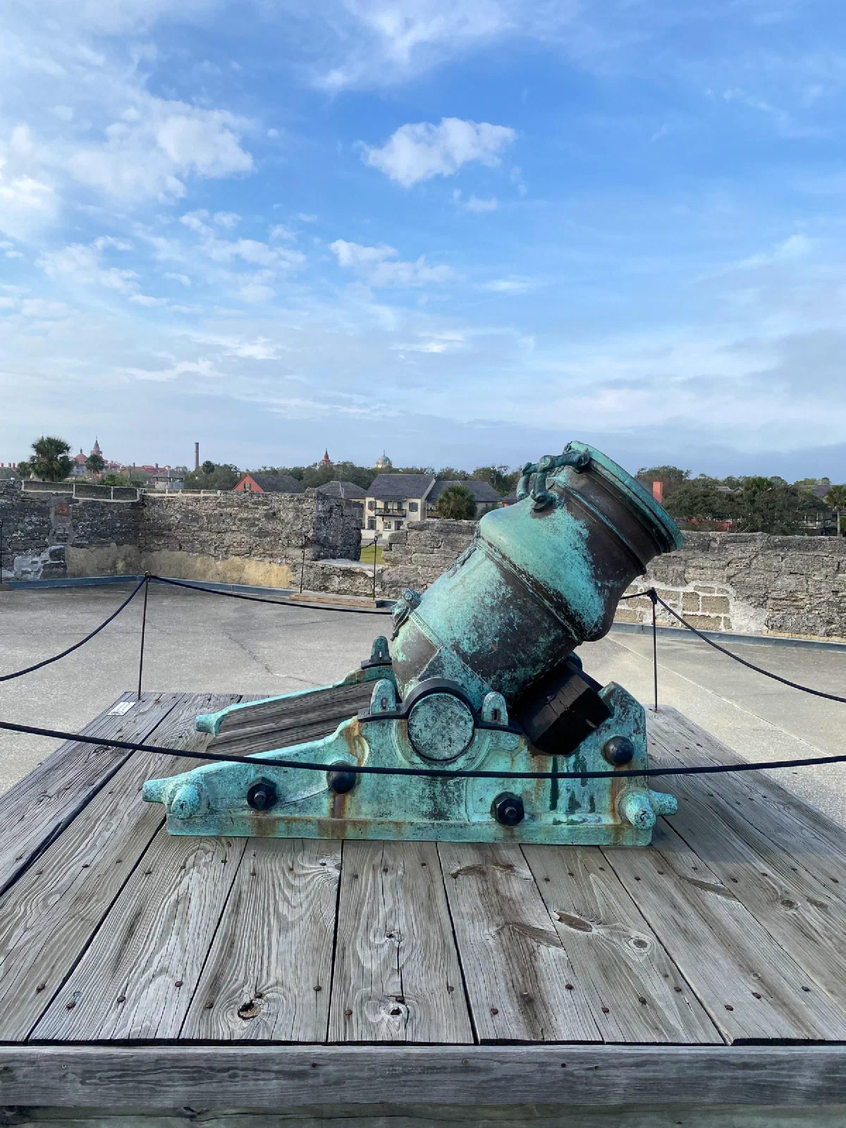 A weathered green cannon mounted on a wooden platform above stone fort walls.