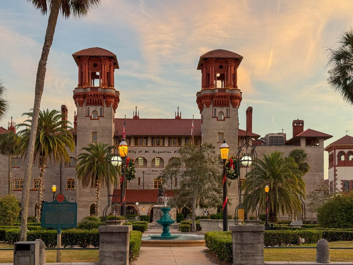 Twin red-roofed towers rising above a courtyard with palms and a fountain.