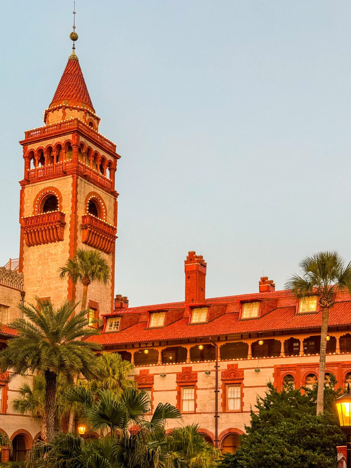 A sunlit orange tower and red-roofed building framed by palm trees.