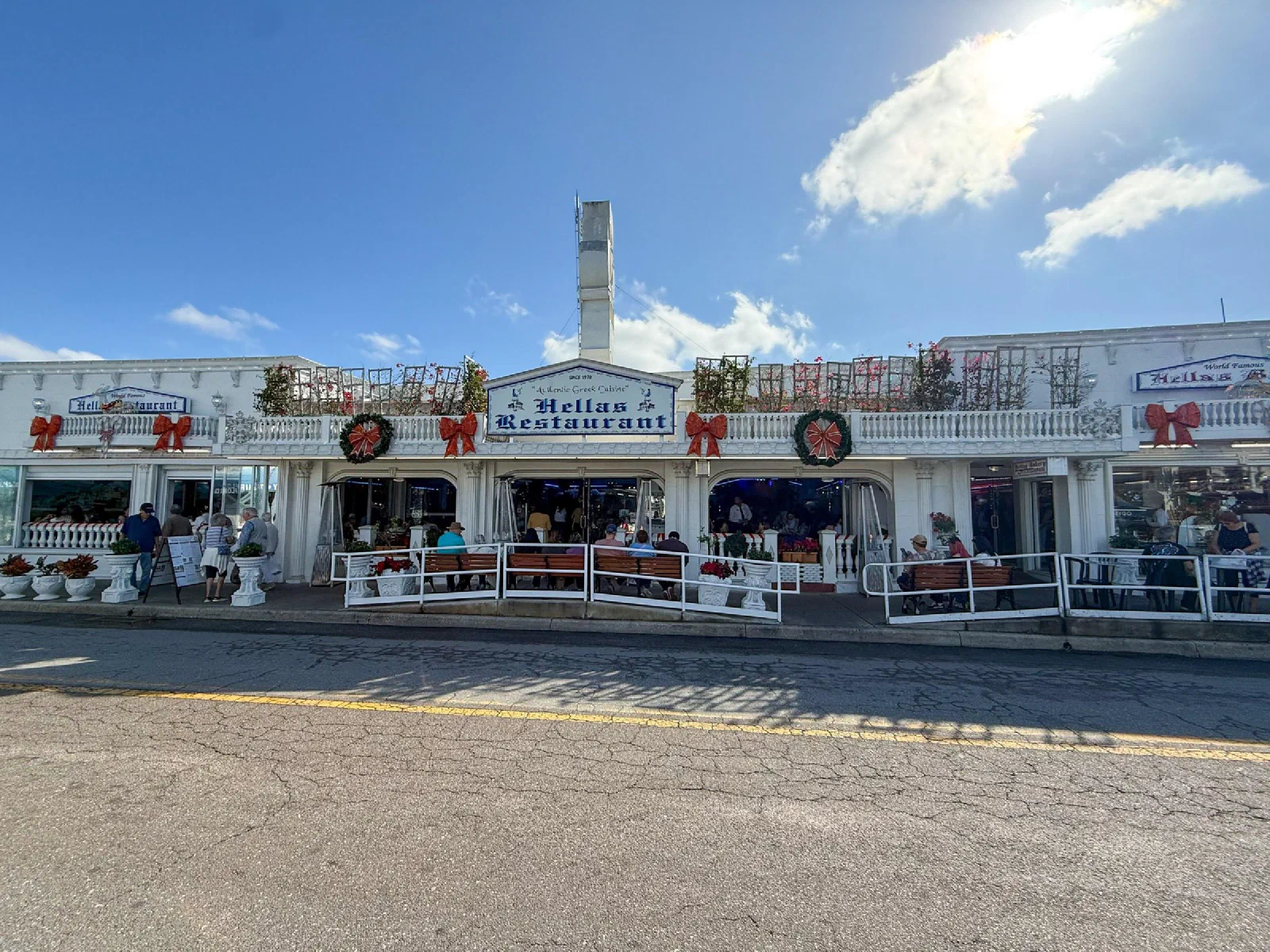 Low waterfront shops with white facades, a restaurant sign, and holiday decorations.